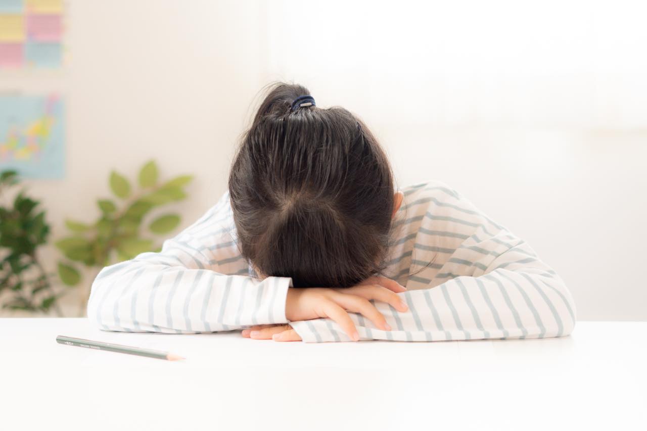 テーブルで勉強に行き詰まって顔を覆う女の子